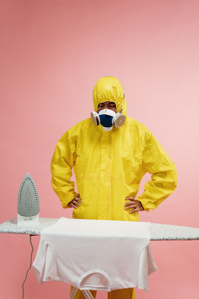 Person in a protective suit humorously ironing clothes, blending safety and daily chores.